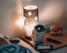 Ozmotic Learning projector resting on a wooden nightstand beside a star-patterned lamp and toy truck, illuminating the room while a child sleeps.