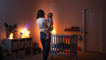 Mother holding her baby in a dimly lit nursery, with the Ozmotic Learning projector casting a soothing blue light from a nearby shelf.
