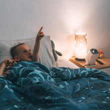 Young boy in a space-themed bed pointing excitedly at a bedtime lesson cast on the ceiling by the Ozmotic Learning projector.