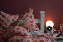 Toddler sleeping peacefully in a strawberry-patterned bed beside the Ozmotic Learning projector and a glowing moon nightlight.